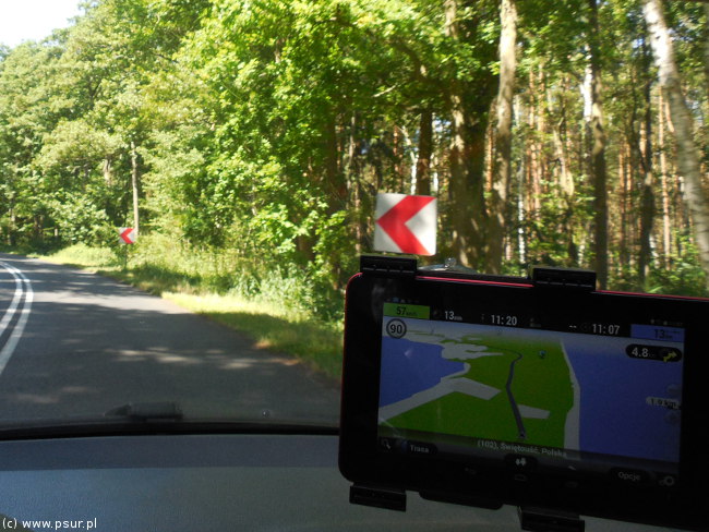 Nawigacja na szybie auta, w tle droga w lesie w słoneczny dzień